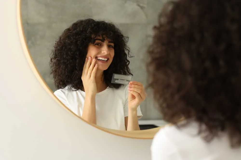 Woman smiling in a mirror holding a whitening strip