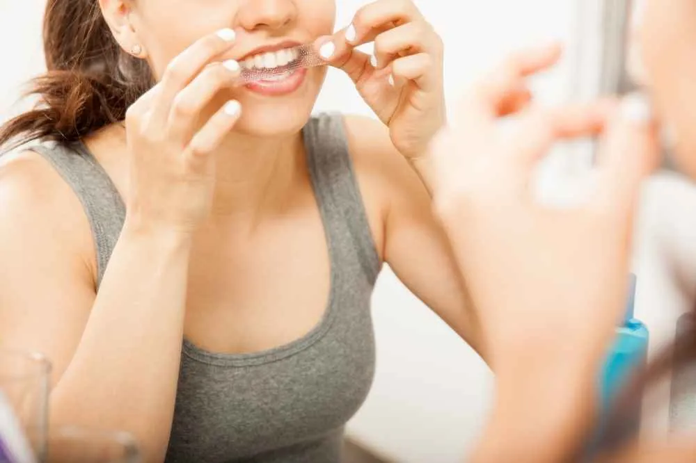 Woman applying a whitening strip in the mirror